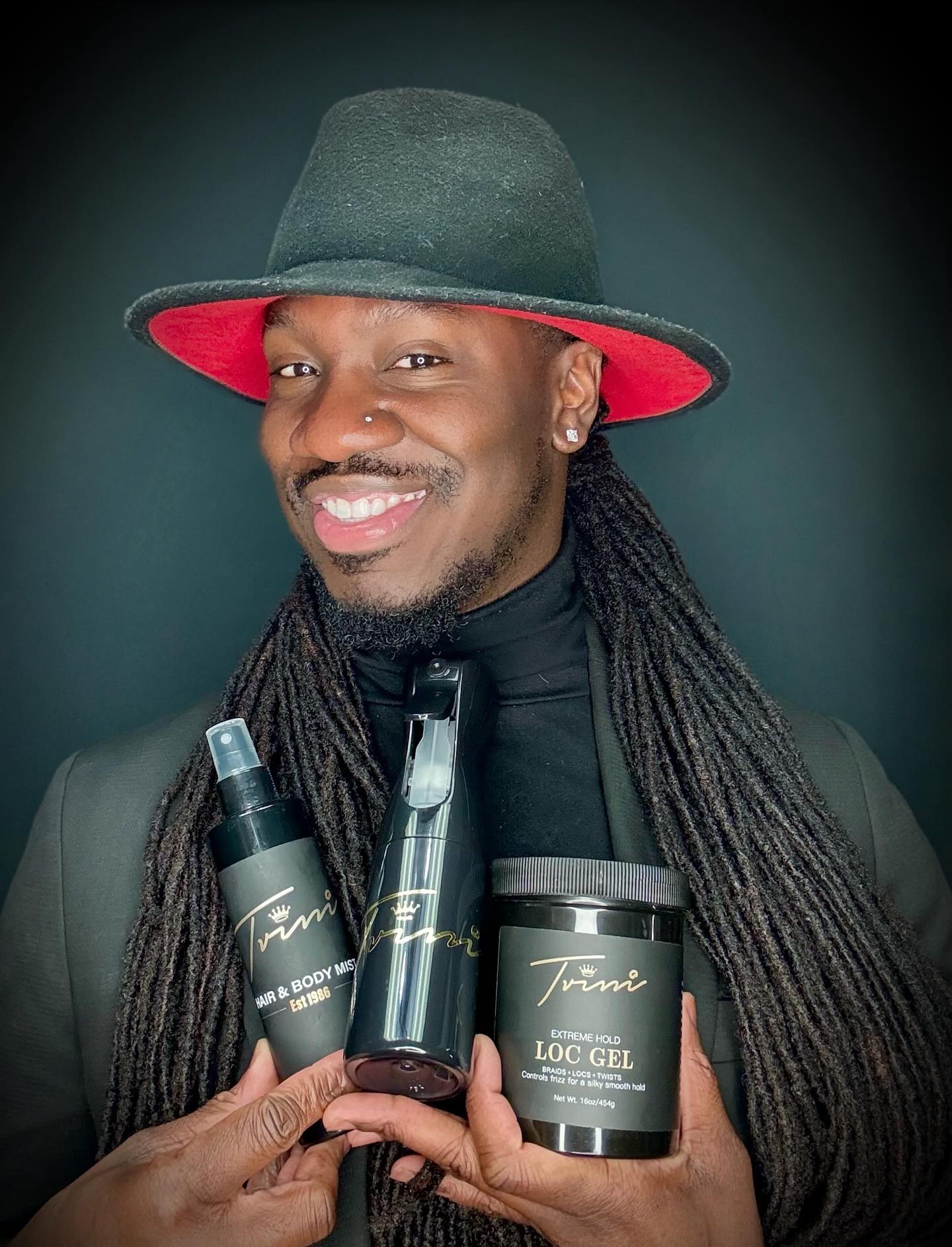 A man with dreadlocks and a hat holding some hair products